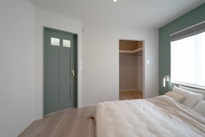 スモーキーグリーンの扉とアクセントクロスでまとめたシンプルなインテリアの寝室